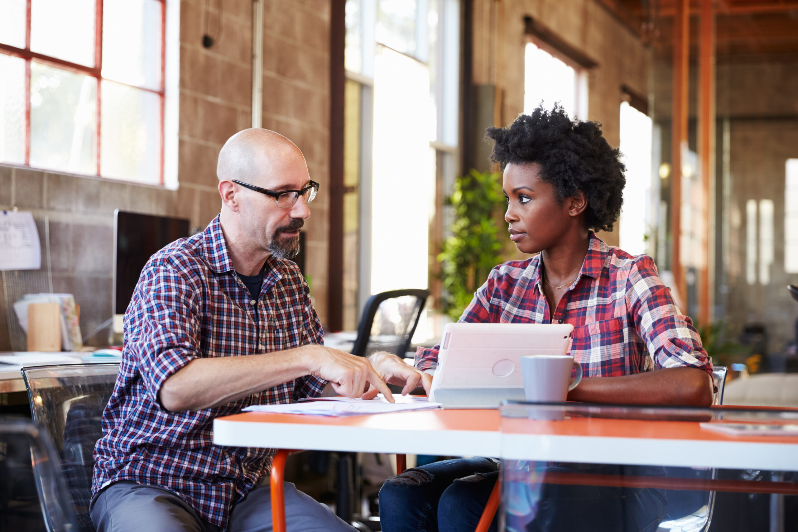 Two,Designers,Sit,At,Meeting,Table,Working,On,Digital,Tablet